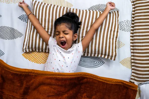 Genç bir çocuk yatakta uyanırken esniyor, parlak bir sabah başlangıcı ve rahat bir atmosfer gösteriyor..