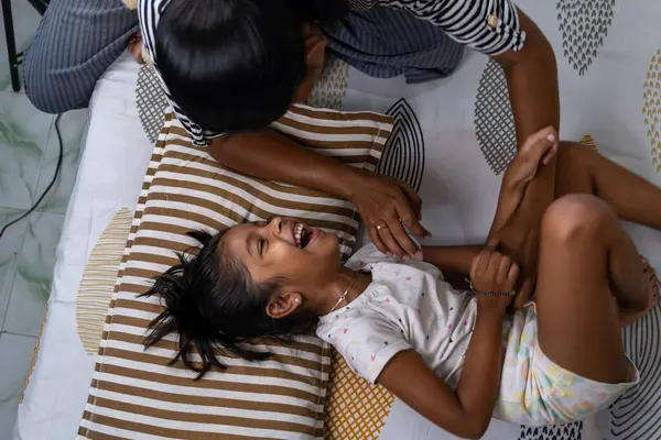 Bir kız, gün boyunca sıcak bir evde bakıcısıyla yatakta oynarken neşeyle güler..