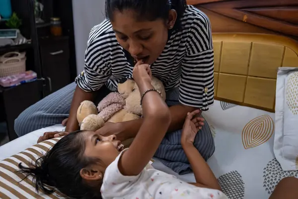 Bir anne, kızıyla samimi bir yatak odasında şakalaşıp kucaklaşır ve doldurulmuş hayvanlarla güler..