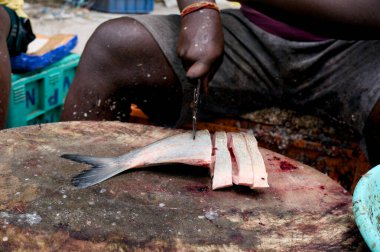 Balıkçı ustalıkla fileto yapar ahşap bir blokta taze yakalanmış bir balığı kalabalık bir pazar gününde..