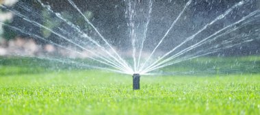 Ev bahçesindeki sulama sistemi. Yeşil çimenleri sulayan otomatik çim püskürtücü. Seçici odak