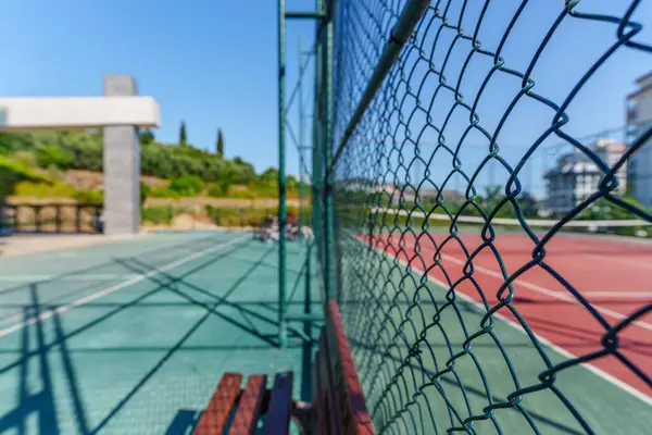 Tahta bir bankın yanında tenis kortunun demir kilidi olan zincirli bir çit.