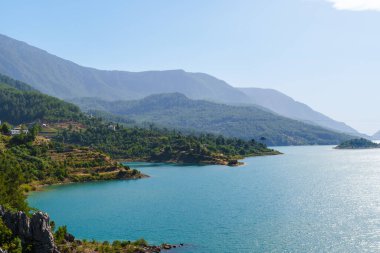 Su barajı ve baraj nehri mavi bulutlu gökyüzünün altındaki yeşil dağlar arasında.