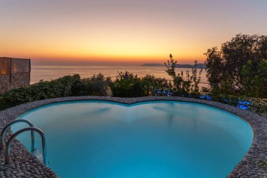 Okyanus üzerinde nefes kesen gün batımı, bereketli bir yamaçtaki lüks sonsuzluk havuzundan görülüyor, huzur ve huzuru çağrıştırıyor..