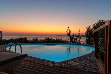 Okyanus üzerinde nefes kesen gün batımı, bereketli bir yamaçtaki lüks sonsuzluk havuzundan görülüyor, huzur ve huzuru çağrıştırıyor..