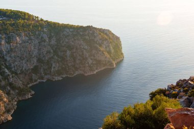 Sersemletici bir günbatımı, sakin Akdeniz üzerinde canlı renkler bırakırken, kayalık uçurumlar sakin sahneyi çerçeveliyor. Huzur ve doğal güzelliği iletmek için mükemmel..