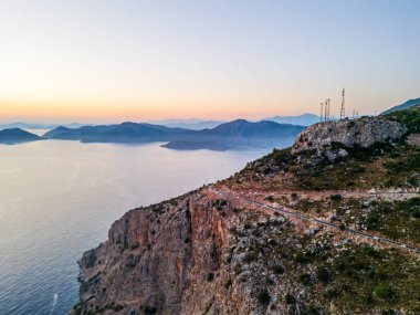 Güneşin doğuşunda sakin okyanusla buluşan kıyı kayalıklarının nefes kesici manzarası ve arka planda dağlar. Huzurlu bir manzara doğanın güzelliğini gösteriyor..
