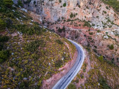 Gün batımında kayalık bir araziyi kesen sarmal bir yolun havadan görünüşü, yemyeşil ve engebeli uçurumlar manzaralı bir manzara yaratır..