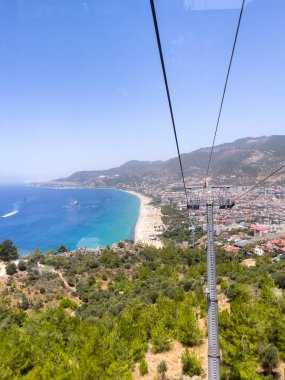 Teleferik manzaralı, deniz üstünde kablolu bir araba, kumsal ve dağlar mavi denizi gösteriyor.