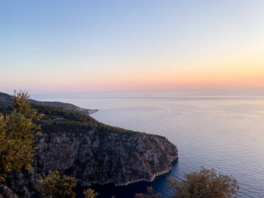 Sahil kayalıklarının sakin mavi okyanusla buluşmasını soluk kesen manzara. Pastel bir günbatımı altında. Huzurlu ve sakin temalar için ideal.