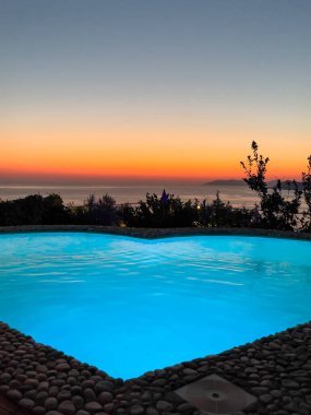 Sakin denize bakan, havuz kenarında parlayan bir günbatımının sakin bir görüntüsü. Renkli gökyüzü dinlenmek için huzurlu bir ortam yaratır..