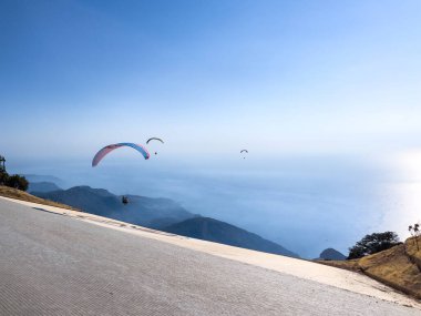 Aydınlık bir günde çarpıcı bir dağ manzarası üzerinde heyecan verici bir uçuşun keyfini çıkaran bir paraglider, macera ve özgürlük sergiliyor..