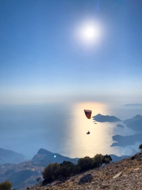 Güneş batarken çarpıcı bir sahil manzarasının üzerinde zarif bir şekilde süzülen bir paraglider denizin ve aşağıdaki adaların üzerine altın rengi döküyor..