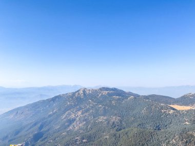 Bir yamaçtan okyanusun nefes kesici panoramik görüntüsü, berrak mavi gökyüzünün altındaki sakin manzarayı yakalıyor..