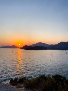 Sakin bir okyanusun üzerinde nefes kesici bir günbatımı manzarası, arka planda görkemli dağlar, sükunetin ve doğal güzelliğin özünü yakalıyor..