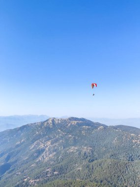 Açık mavi gökyüzünün altında yüksekte uçan ve macera ve özgürlüğün özünü yakalayan bir paraglider 'ın nefes kesici bir sahnesi..