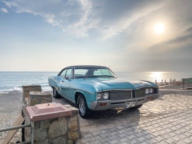 Sahilde mavi gökyüzü olan klasik bir arabanın sahnesi.