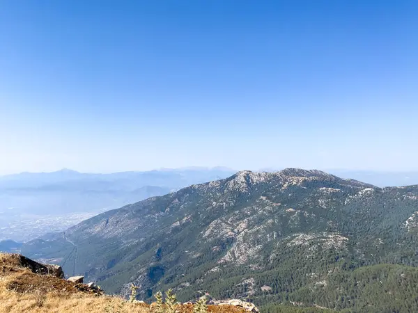 Bir yamaçtan okyanusun nefes kesici panoramik görüntüsü, berrak mavi gökyüzünün altındaki sakin manzarayı yakalıyor..