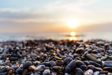 Okyanusun üzerinde güzel bir günbatımı ön planda parıldayan çakıl taşlarıyla doğal güzelliğin sakin ve sakin bir atmosferini yaratıyor..
