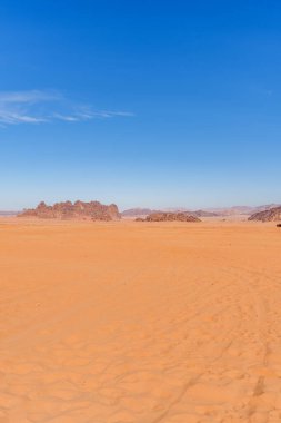 A stunning desert landscape featuring orange sand dunes, rugged rocky outcrops, and a vibrant blue sky adorned with delicate white clouds, showcasing the beauty and vastness of desert wilderness. clipart