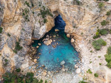 Stunning aerial shot of a hidden cove with turquoise waters, surrounded by rugged cliffs and a natural rock arch. Perfect for exploring nature's beauty and tranquil coastal scenes. clipart