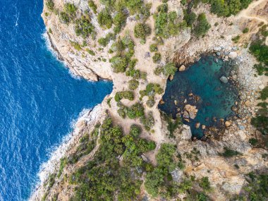 Parlak mavi suları ve yemyeşil yaprakları olan engebeli bir sahil şeridinin sersemletici görüntüsü, yukarıdan doğanın güzelliğini ve sükunetini gösteriyor..