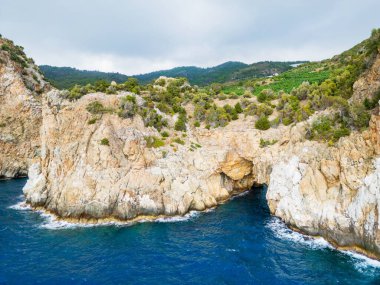 A stunning view of rugged cliffs and lush greenery meeting the vibrant blue sea. Captures the beauty and tranquility of coastal landscapes, offering a sense of adventure and serenity. clipart