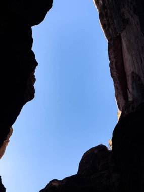 Parlak güneş ışığı altında heybetli, sarp kayalık bir kanyonun duvarları tarafından çerçevelenmiş berrak mavi bir gökyüzü dramatik ve nefes kesici bir görsel yaratıyor.