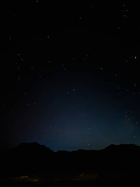 Siluetli bir dağ sırasının üzerindeki yıldızlı bir gecenin sakin manzarası huzur ve kozmik bir mucizeyi taşıyor..