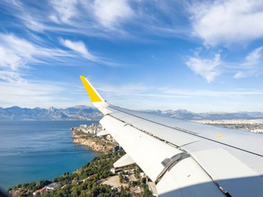 In-flight view showcasing an airplane wing against a bright blue sky, overlooking an expansive ocean with mountainous landscapes visible in the distance. The perspective conveys a sense of travel, exploration, and wanderlust. clipart