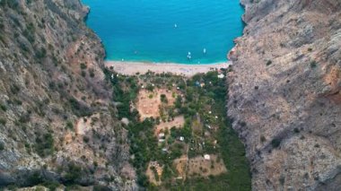 Koyda tekneleri olan ve iki dağ arasında kayıkları hareket ettiren bir kumsal görüntüsü.