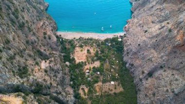 Koyda tekneleri olan ve iki dağ arasında kayıkları hareket ettiren bir kumsal görüntüsü.