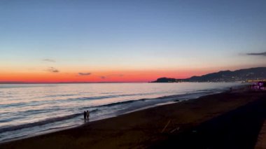 Canlı bir gün batımının manzarası okyanusu aydınlatıyor ve huzurlu bir sahil atmosferi yaratıyor.
