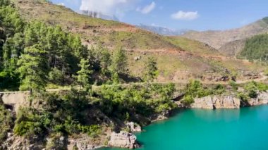 Alanya, Antalya 'daki mavi bulutlu gökyüzünün altında yeşil dağlarla çevrili yeşil ağaçların arkasındaki loş bir nehir ve barajın görüntüleri.