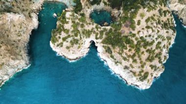 Okyanusta kayalık bir dağın yanında doğal su mağarası oluşumunu gösteren hava aracı görüntüsü.