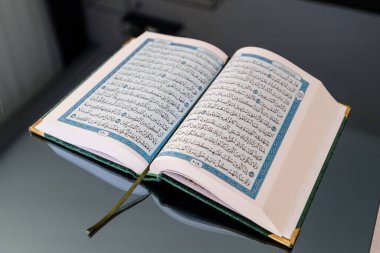 Yansıtıcı bir yüzeye yerleştirilmiş karmaşık mavi ve altın dekoratif detaylara sahip güzel Arapça yazılar içeren açık bir Kur 'an kitabı..