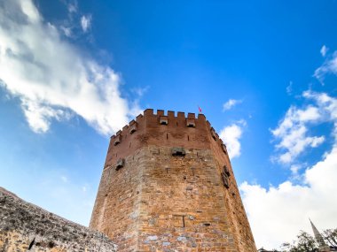 Belirgin bir kule ve heykel barındıran tarihi mimari, canlı mavi gökyüzünün altında tuhaf evler ve ağaçlarla çevrili bir tepe..