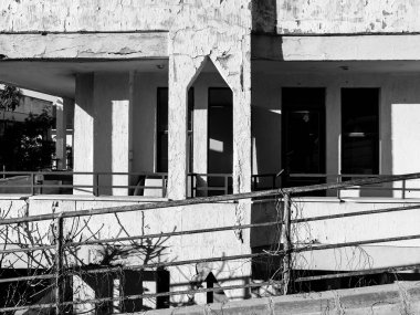 Terk edilmiş bina cephesi, kırık pencereler ve hasarlı yapılar, çürüme ve geçmişteki araç gerilimini çağrıştırıyor.