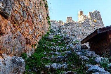 Tarihi bir şatonun kalıntılarına doğru yükselen antik bir taş yolun görüntüsü, parlak mavi gökyüzünün altındaki yeşil tamamlanmış taş duvarların canlı dokularını gözler önüne seriyor..