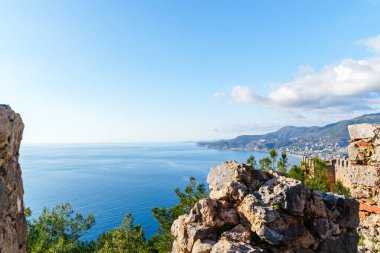 Türkiye 'nin Alanya Şatosu' ndan canlı mavi bir okyanus, yemyeşil ve engebeli kayalık bir çıkıntıdan görülen uzak tepelerin nefes kesici güzelliği..