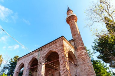 Kırmızı tuğladan yapılmış tarihi bir cami, kemerli bir galeri, ve uzun bir minare, doğal güneş ışığıyla yıkanmış ve ağaçlarla çevrili, dingin bir mimari ve kültürel ortam yaratıyor..