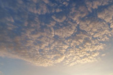 Dağınık bulutların büyüleyici görüntüsü mavi gökyüzüne karşı altın renginde aydınlatılıyor, sakin ve sakin bir atmosferi çağrıştırıyor. Doğa, huzur ve rüya gibi manzaralar için mükemmel..