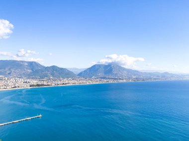 Turkuaz suların, dağların ve hareketli bir kasabanın bulunduğu çarpıcı bir kıyı şeridinin panoramik manzarası. Huzuru, doğal güzelliği ve manzaralı deniz manzaralarını tasvir etmek için mükemmel bir sahne..