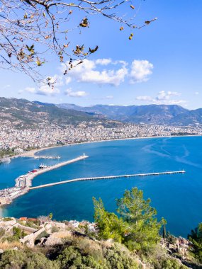 Turkuaz suların, dağların ve hareketli bir kasabanın bulunduğu çarpıcı bir kıyı şeridinin panoramik manzarası. Huzuru, doğal güzelliği ve manzaralı deniz manzaralarını tasvir etmek için mükemmel bir sahne..