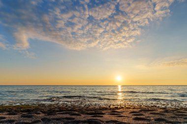 Yumuşak bulutlu bir gökyüzü altında okyanus dalgalarına yansıyan, huzur veren ve rahatlatıcı bir atmosfer sunan, altın ışıklarla dolu bir deniz batımı sahnesi..
