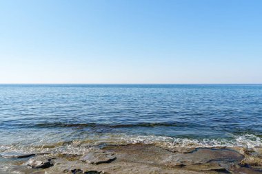 Sakin bir denizle buluşan kayalık bir kıyı şeridinin huzurlu görüntüsü