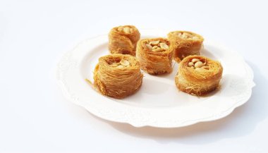 Yerfıstıklı yuvarlak bir baklava, ortada beyaz bir tabakta beyaz bir zemin