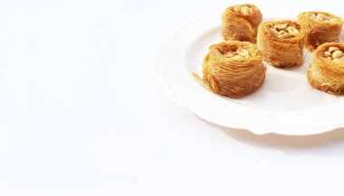 Fıstıklı yuvarlak bir baklava, beyaz bir tabakta ve beyaz bir arka planda