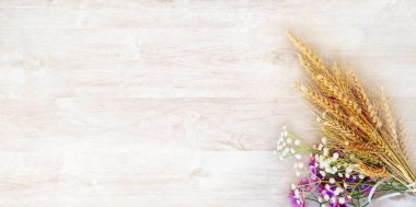 Beyaz ahşap bir yüzeyde mor ve beyaz çiçekli olgun sarı buket. Shavuot bayramı için bir tebrik kartı.