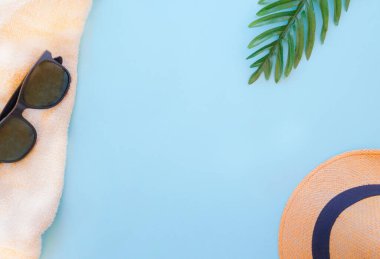 Tatil aksesuarları, şapka, güneş gözlüğü, havlu, mavi arka planda avuç içi. Denizde veya yüzme havuzunda. Tropikal bir atmosferde yaz tatili. Metin için boş alan. Yakında dönerim. İyi tatiller.